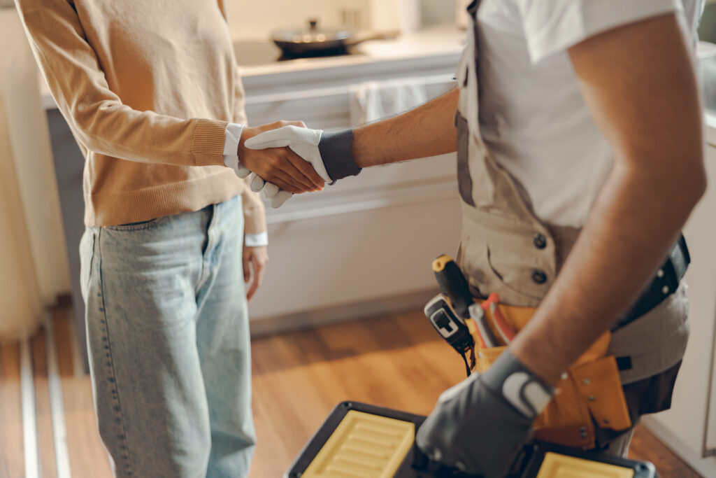 How to Sell my House Warner Robins: rClose up of repairman in uniform shaking hands with woman while standing at home kitchen